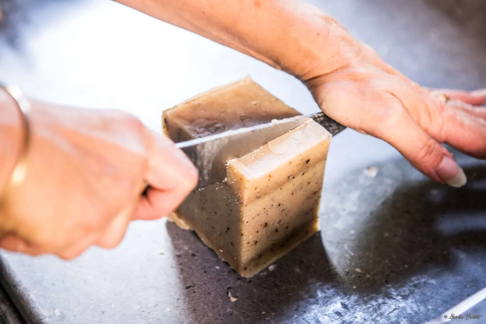 Coupe à la main d'un pain de savon saponifié à froid, au labo de Petite-Île